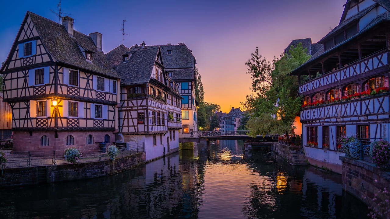 Quaint half-timbered houses along a serene canal in Strasbourg, France, during sunset.